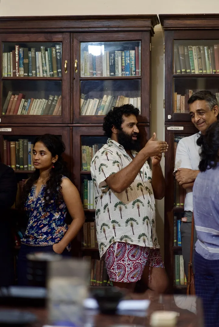 A conversation among guests beside coffee samples and the club bookshelves.