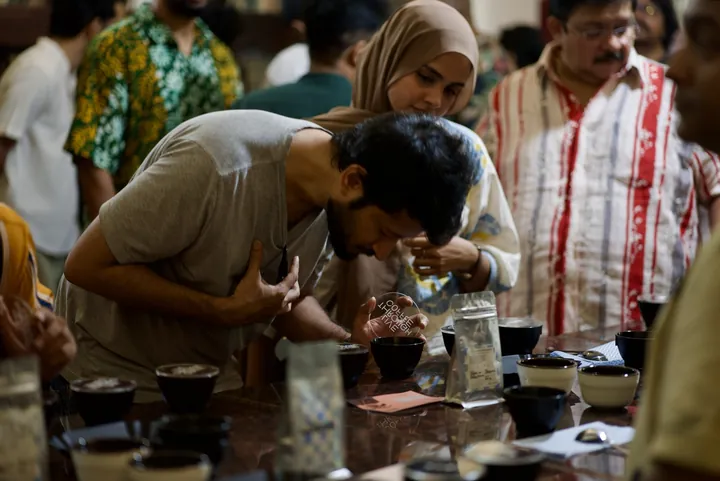 A participant tasting coffee from a cupping spoon as other guests explore the samples.