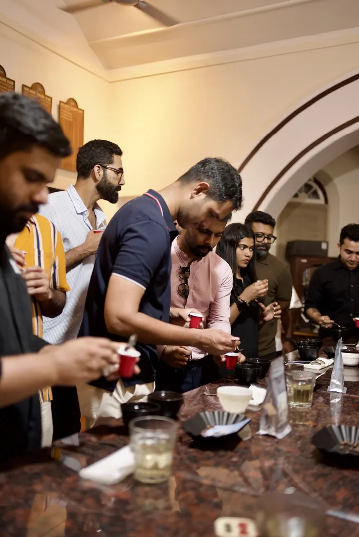 A group sampling coffees with red cups and cupping spoons at the Kochi gathering.