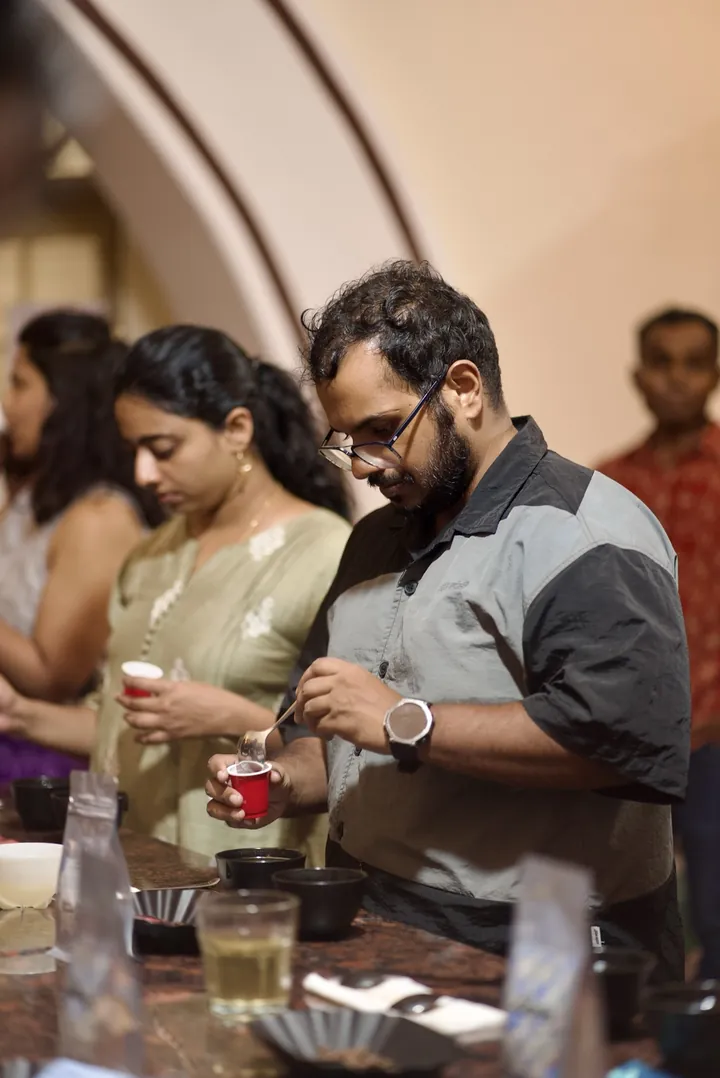 A participant holding a cupping spoon above a red sample cup during the tasting.